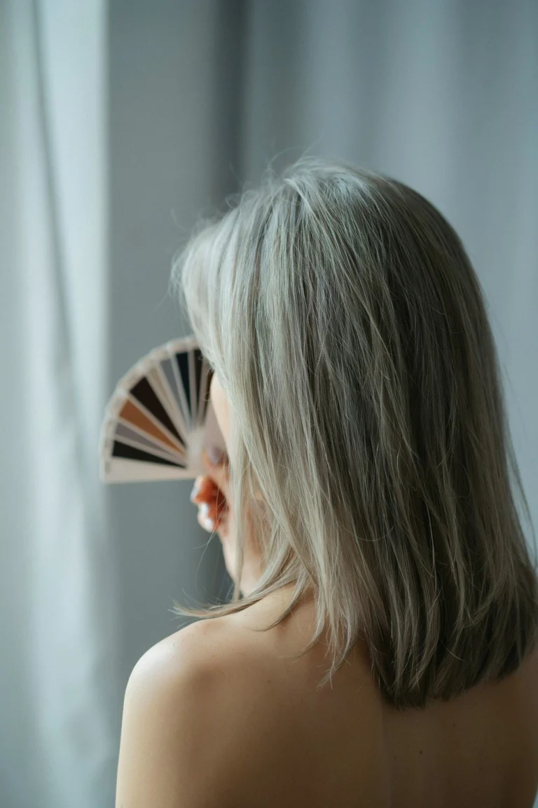 A swatch ring of silver and grey shades fanned beside a section of grey hair in soft light