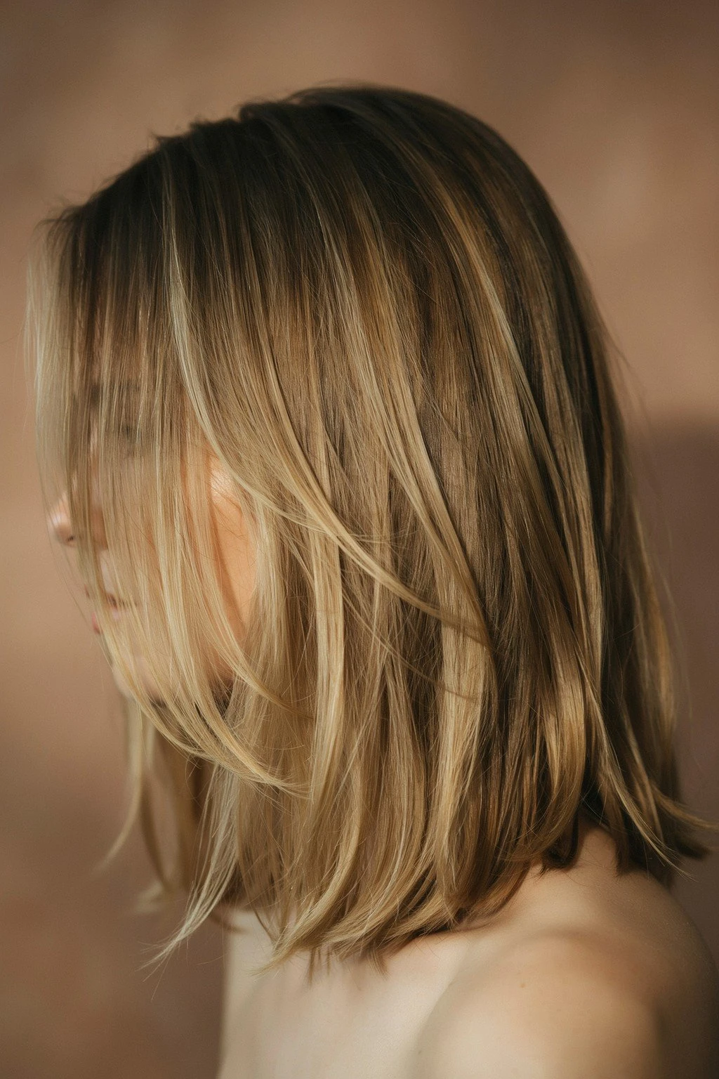 Dark brown hair with soft golden blonde pieces woven through the mid-lengths, warm light catching the contrast