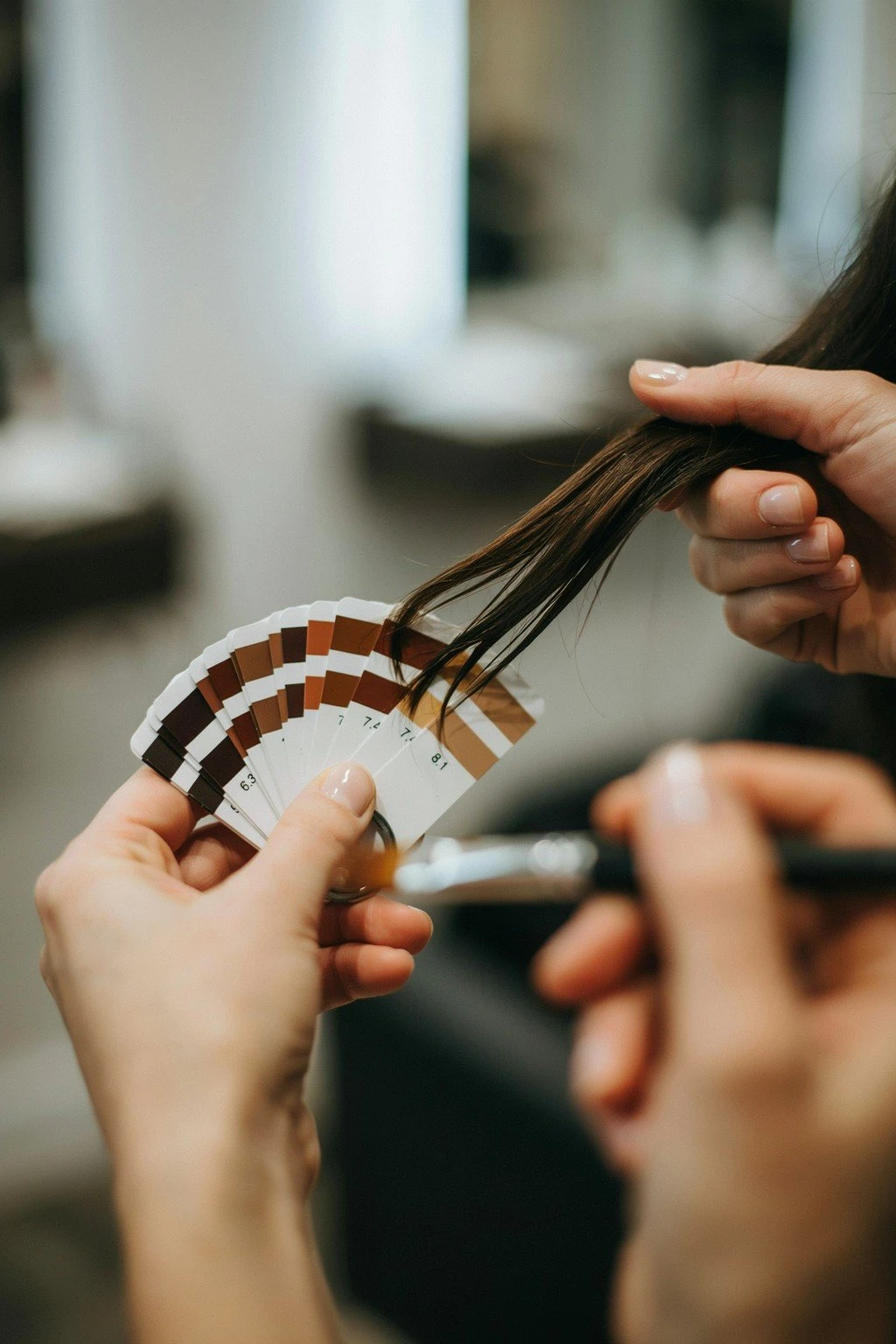 A colorist's ring of level swatch cards in browns and caramels held beside a section of dark brunette hair