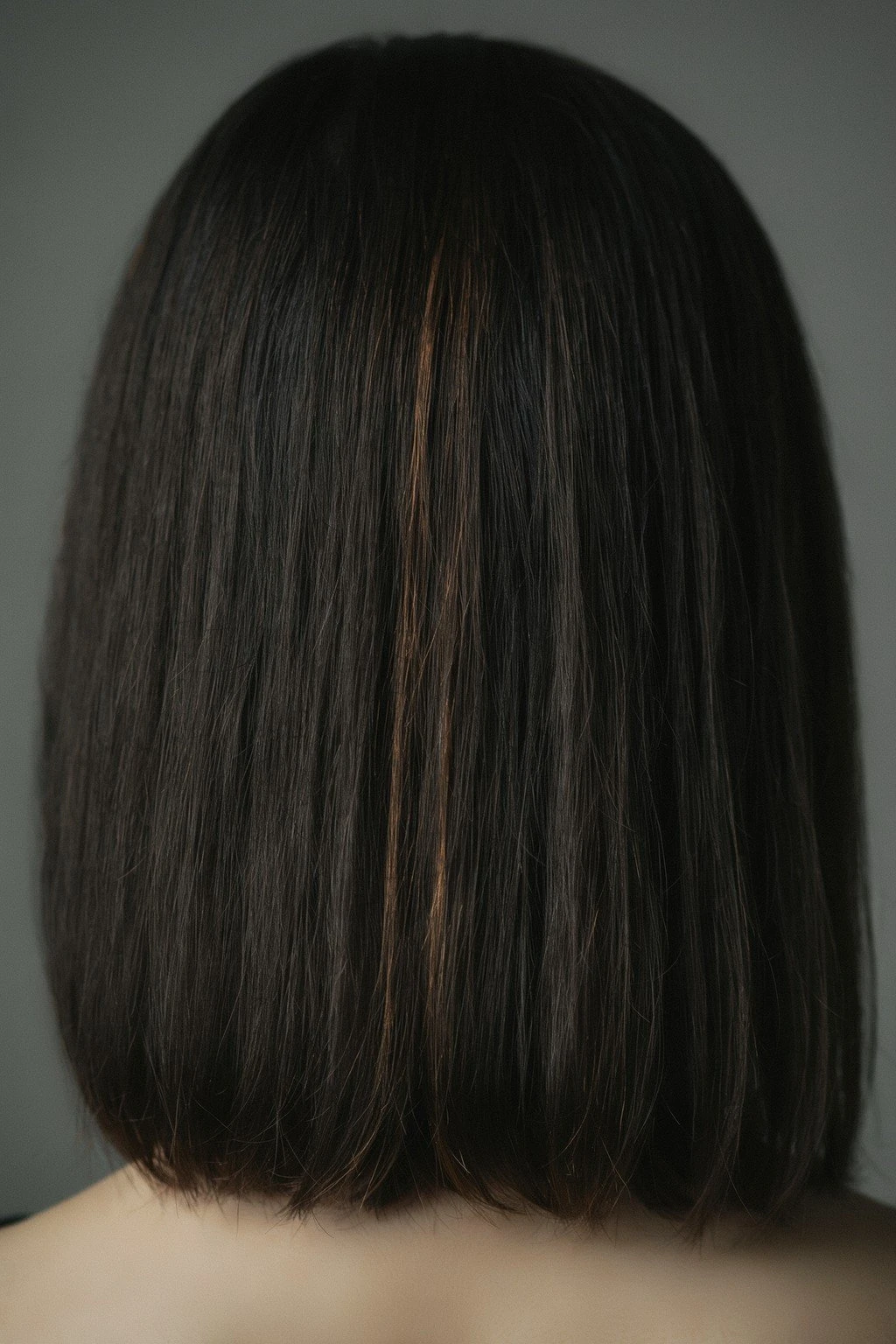 Jet black hair with subtle warm caramel pieces catching the light along the mid-lengths, the base still reading almost entirely black