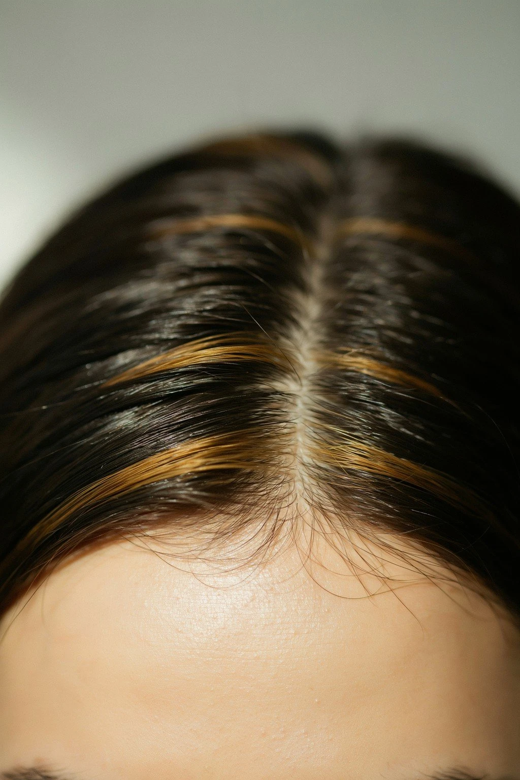 Close crop of face-framing caramel highlight pieces at the hairline of dark brunette hair, the rest of the head implied and out of focus