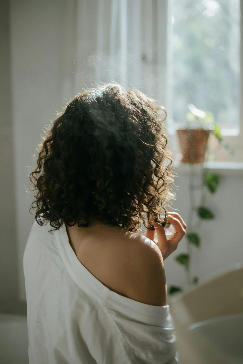 Woman refreshing curly hair with a light water spritz