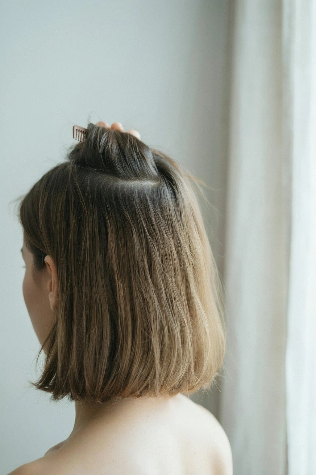 A section of hair lifted near a bright window, natural light falling on the root area to show its true depth