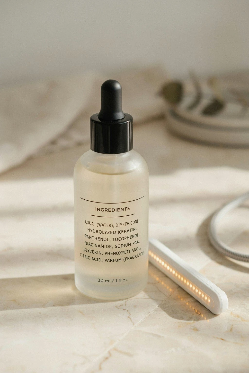 Close-up of an ingredient list on a hair serum bottle beside a small at-home laser device