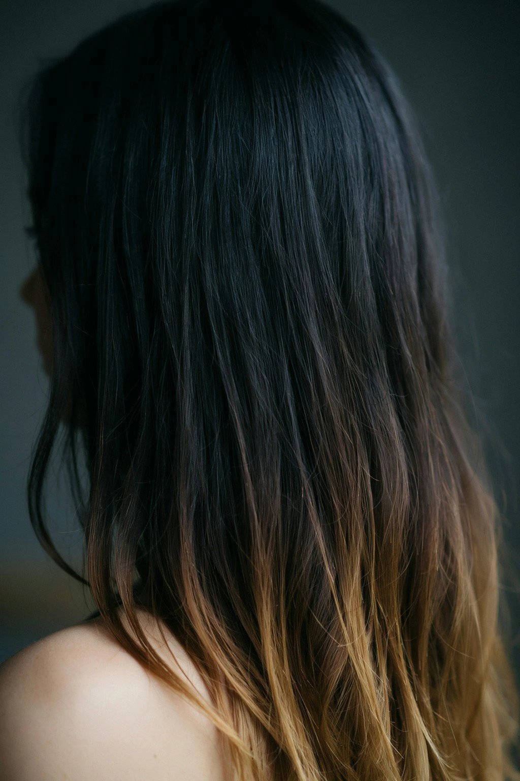 Jet black hair melting into warm caramel through the last several inches, the transition soft and low in the frame
