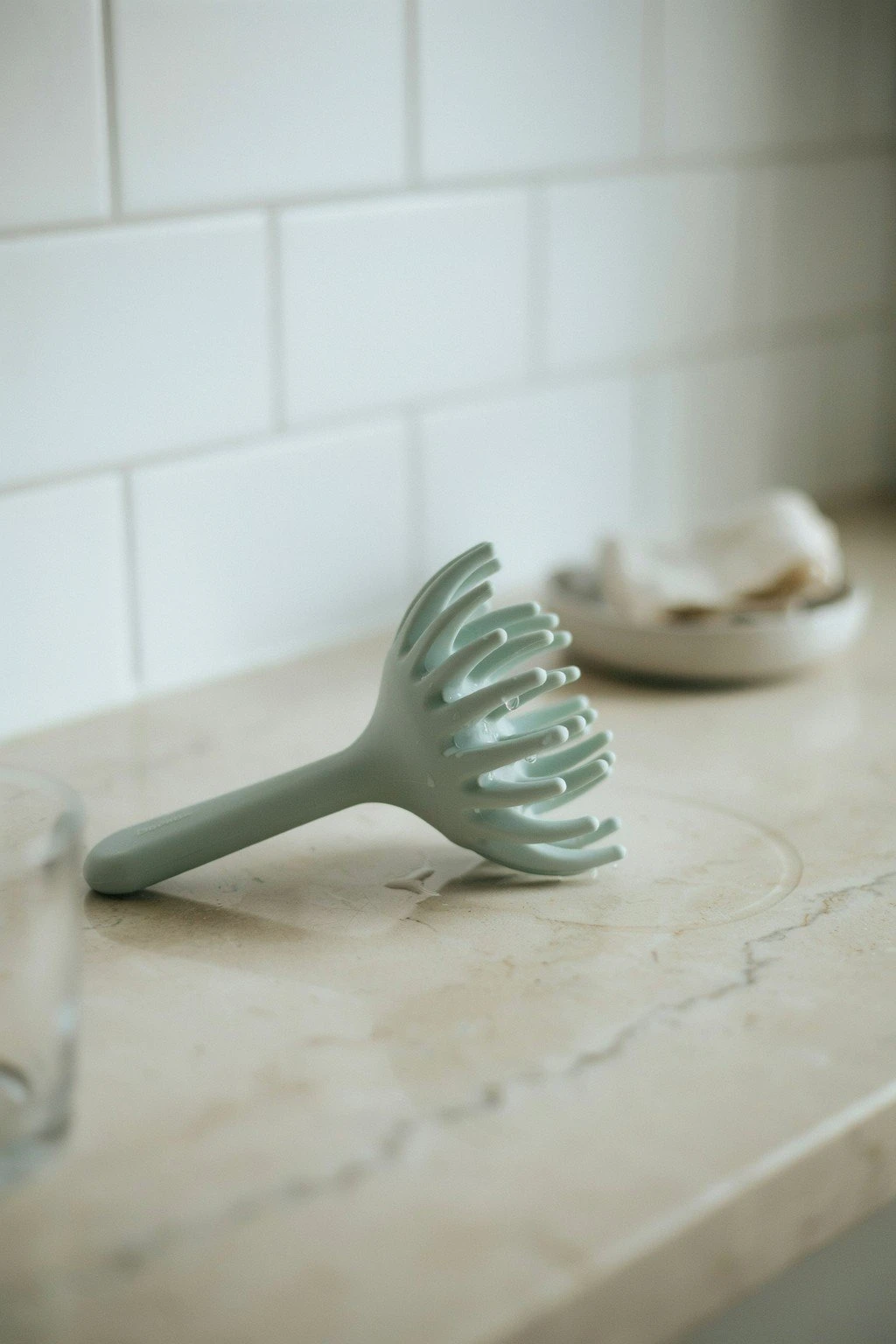 A handheld silicone scalp massager resting on a bathroom counter