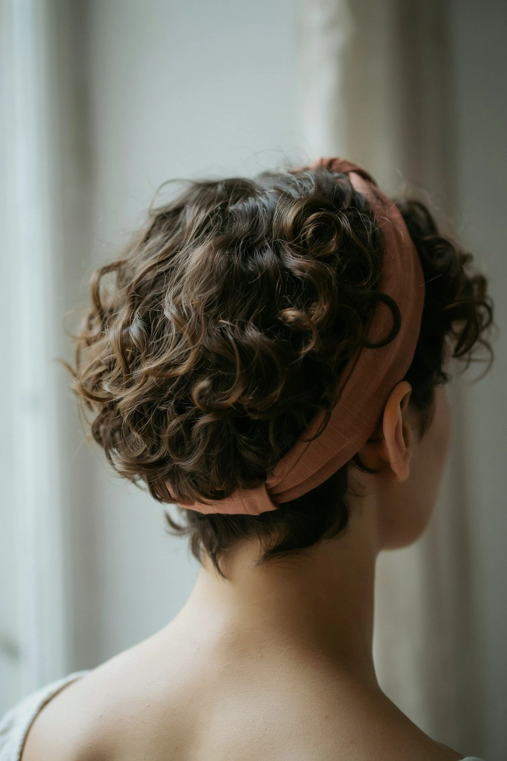 Woman with a short curly haircut featuring a headband and defined curls